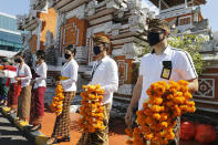 Airport officers wearing face masks line up as they hold flowers to welcome passengers at Bali airport, Indonesia on Friday, July 31, 2020. Indonesia's resort island of Bali reopened for domestic tourists after months of lockdown due to a new coronavirus. (AP Photo/Firdia Lisnawati)