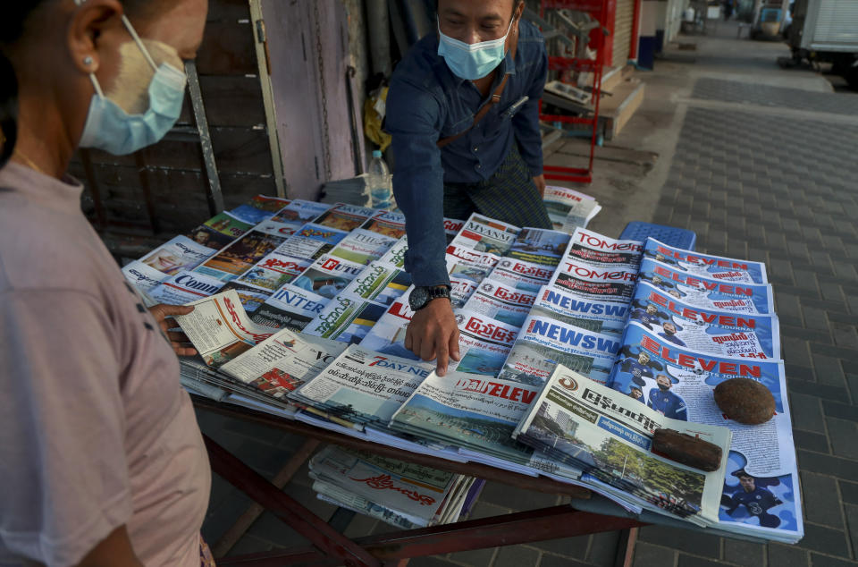 A newspaper seller points at a front-page of a newspaper in Yangon, Myanmar, Tuesday, Feb. 2, 2021. Hundreds of members of Myanmar's Parliament remained confined inside their government housing in the country's capital on Tuesday, a day after the military staged a coup and detained senior politicians including Nobel laureate and de facto leader Aung San Suu Kyi. (AP Photo/Thein Zaw)