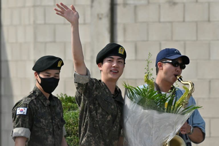 Jin (c), membre du boys band BTS, salue après avoir été libéré de son service militaire à côté des autres membres RM (d) et Jimin (g) à l'extérieur du camp d'entraînement de Yeoncheon, en Corée du Sud, le 12 juin 2024 (Jung Yeon-je)