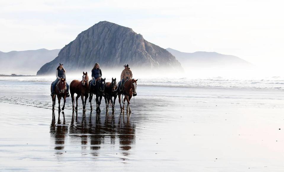 Framed by Morro Rock, Cal Poly students Lyndsey Goldwyn, left, Sydney Goldwyn and Taylor Marrou exercise their horses on the beach during a break in wet weather on Jan., 6, 2023.