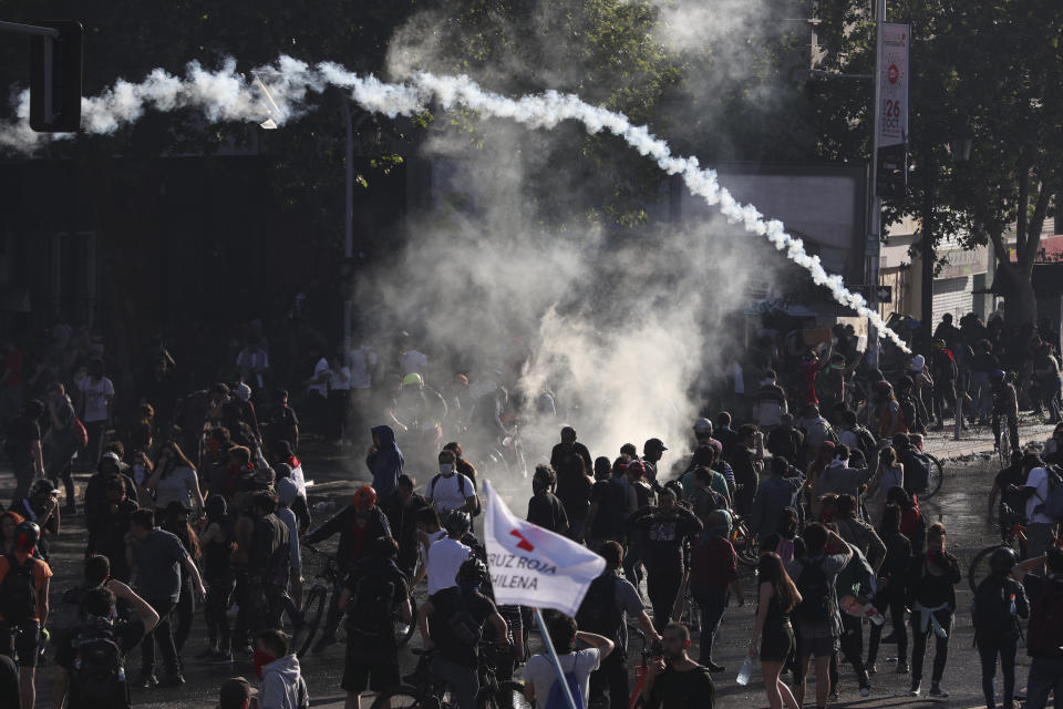 Demonstrators clash with police launching tear gas as a state of emergency remains in effect in Santiago, Chile, Sunday, Oct. 20, 2019. Protests in the country have spilled over into a new day, even after President Sebastian Pinera cancelled the subway fare hike that prompted massive and violent demonstrations. (AP Photo/Esteban Felix)