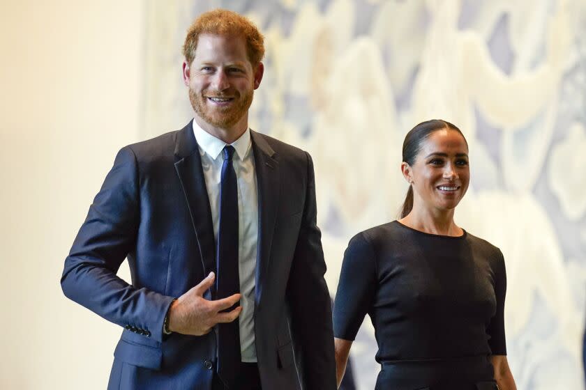 A smiling man in a blue suit holds hands with a smiling woman in a black dress