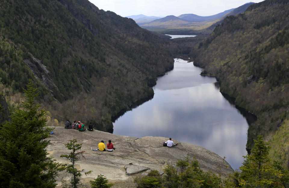 Hikers take in the view of Lower Ausable Lake from Indian Head Summit, Saturday, May 15, 2021, at the Adirondack Mountain Reserve near St. Huberts, N.Y. A free reservation system went online recently to control the growing number of visitors packing the parking lot and tramping on the trails through the private land of the Adirondack Mountain Reserve. The increasingly common requirements, in effect from Maui to Maine, offer a trade-off to visitors, sacrificing spontaneity and ease of access for benefits like guaranteed parking spots and more elbow room in the woods. (AP Photo/Julie Jacobson)