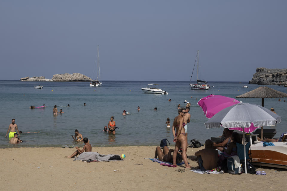 FILE - Tourists enjoy the beach and the sea in Lindos, on the Aegean Sea island of Rhodes, southeastern Greece, on Thursday, July 27, 2023. Tourists at a seaside hotel on the Greek island of Rhodes snatched up pails of pool water and damp towels as flames approached, rushing to help staffers and locals extinguish one of the wildfires threatening Mediterranean locales during recent heat waves. (AP Photo/Petros Giannakouris, File)