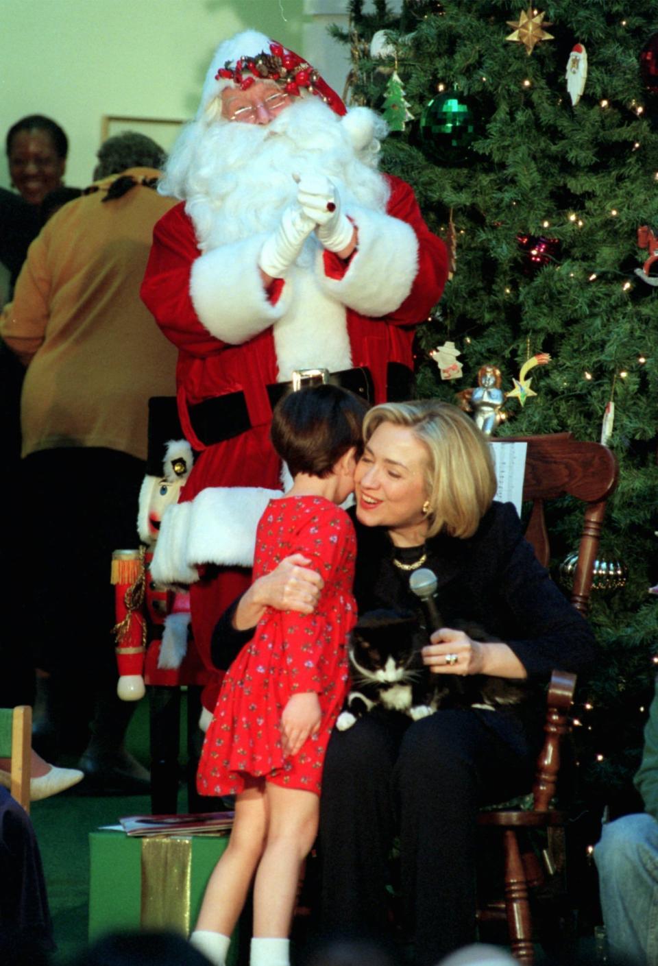 Santa Claus and Socks looks on as first lady Hillary Rodham Clinton hugs Katherine Meinhardt, 7, of Mechanicsville, Md. during Mrs. Clinton's annual visit to Children's National Medical Center in Washington Tuesday Dec. 16, 1997. (AP Photo/Dennis Cook)