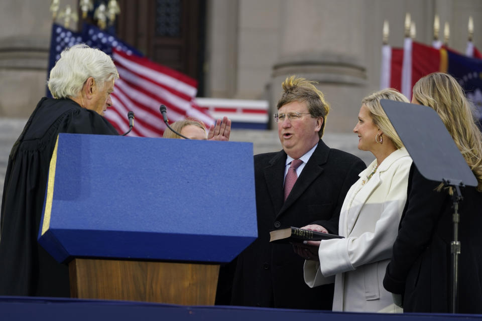 A strong wind blows across the Mississippi State Capitol grounds as Mississippi Republican Gov. Tate Reeves, center, recites the oath of office as given to him by Mississippi Supreme Court Chief Justice Michael Randolph, left, while his wife Elee Reeves, right, holds the family Bible during the inauguration ceremony in Jackson, Miss., Tuesday, Jan. 9, 2024. (AP Photo/Rogelio V. Solis)