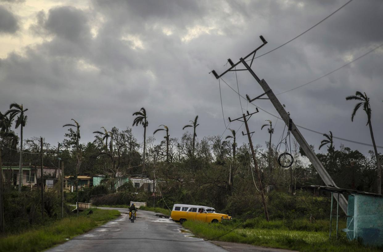 A classic American car drives past utility poles tilted by Hurricane Ian in Pinar del Rio, Cuba, Tuesday, Sept. 27, 2022.