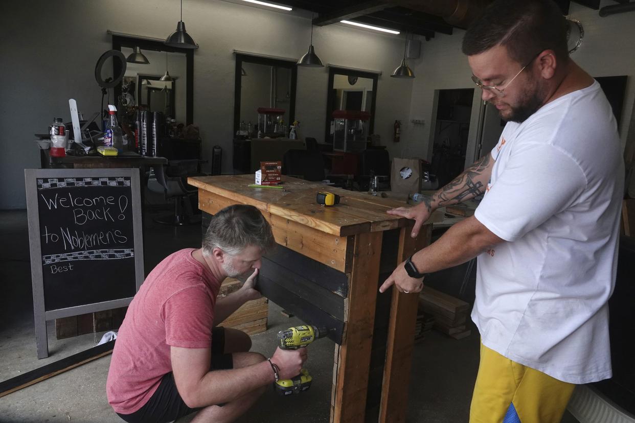Greg Young, right, owner of Nobleman's Cut & Shave in Fort Lauderdale's Fat Village, modifies his shop to observe social distancing, with the help of his friend Jay Weaver on Sunday, May 17, 2020. Broward County businesses are set to partially reopen Monday morning.