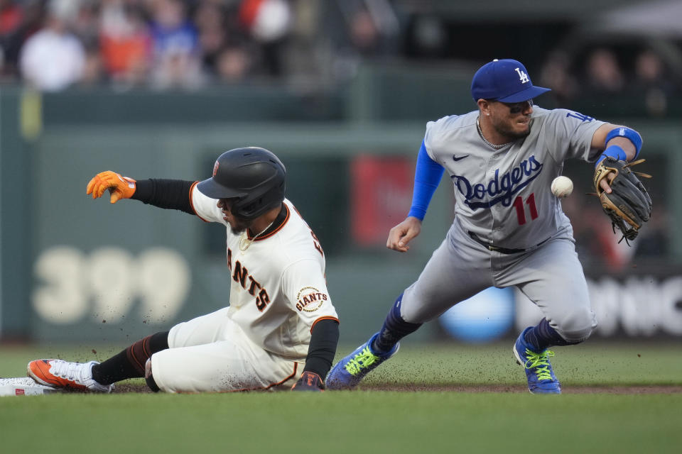 San Francisco Giants' Thairo Estrada, left, reaches second as Los Angeles Dodgers shortstop Miguel Rojas is unable to catch the throw from right fielder Mookie Betts during the first inning of a baseball game in San Francisco, Wednesday, April 12, 2023. Wilmer Flores singled on the play. (AP Photo/Godofredo A. Vásquez)