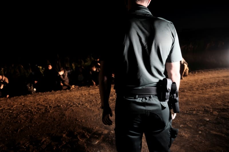 Latvian border guard looks at detained migrants next to the Belarus-Latvia border near Vorzova