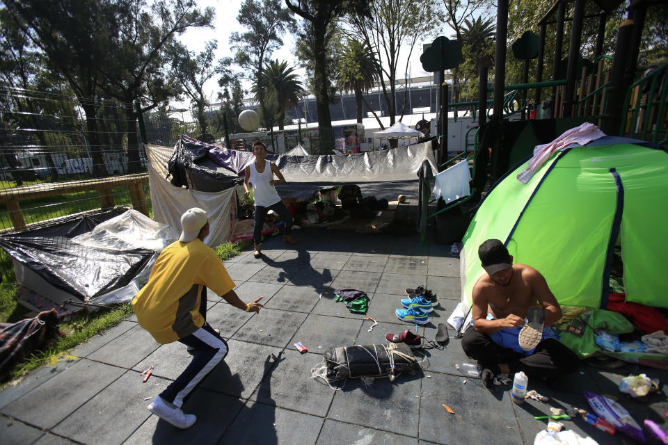 Central American migrants who are part of a group from different countries who banded together on their journey north for safety, and pooled their money to buy two tents, play with a soccer ball as another scrubs his shoes clean with a toothbrush, at the sports complex where thousands of migrants have been camped out for several days in Mexico City, Friday, Nov. 9, 2018. About 500 Central American migrants headed out of Mexico City on Friday to embark on the longest and most dangerous leg of their journey to the U.S. border, while thousands more were waiting one day more at a massive improvised shelter. (AP Photo/Rebecca Blackwell)