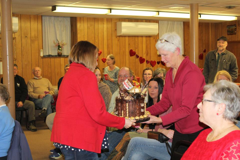 Pam Walukas and Judy Miller take Miranda Durst's cake Who Needs Gravity around to show the bidders at Death By Chocolate in Meyersdale on Friday evening.