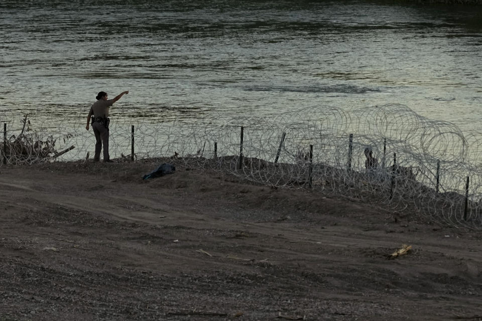 A Texas state trooper talks with migrants as they walk along concertina wire on the banks of the Rio Grande as they try to enter the U.S. from Mexico in Eagle Pass, Texas, Thursday, July 6, 2023. Texas Republican Gov. Greg Abbott has escalated measures to keep migrants from entering the U.S. He's pushing legal boundaries along the border with Mexico to install razor wire, deploy massive buoys on the Rio Grande and bulldozing border islands in the river. (AP Photo/Eric Gay)