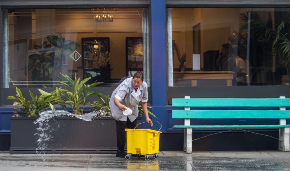 A woman carefully cleans the sidewalk outside the Hotel Atwater in Avalon, CA.