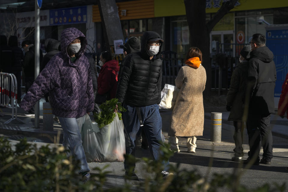 A couple carrying a bag of groceries walk by residents who line up in freezing cold temperatures for their routine COVID-19 throat swabs at a coronavirus testing site in Beijing, Sunday, Dec. 4, 2022. China on Sunday reported two additional deaths from COVID-19 as some cities move cautiously to ease anti-pandemic restrictions amid increasingly vocal public frustration over the measures. (AP Photo/Andy Wong)