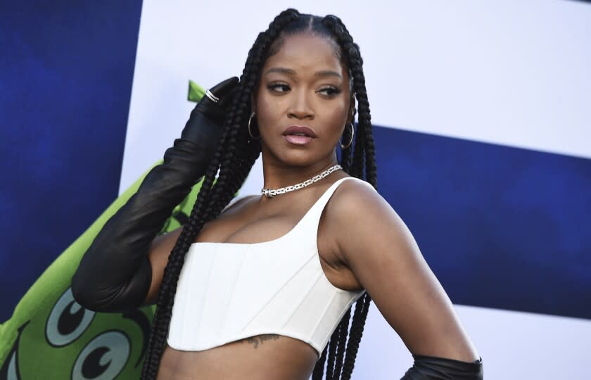 A woman with long, braided hair posing in a white crop top and silver necklace