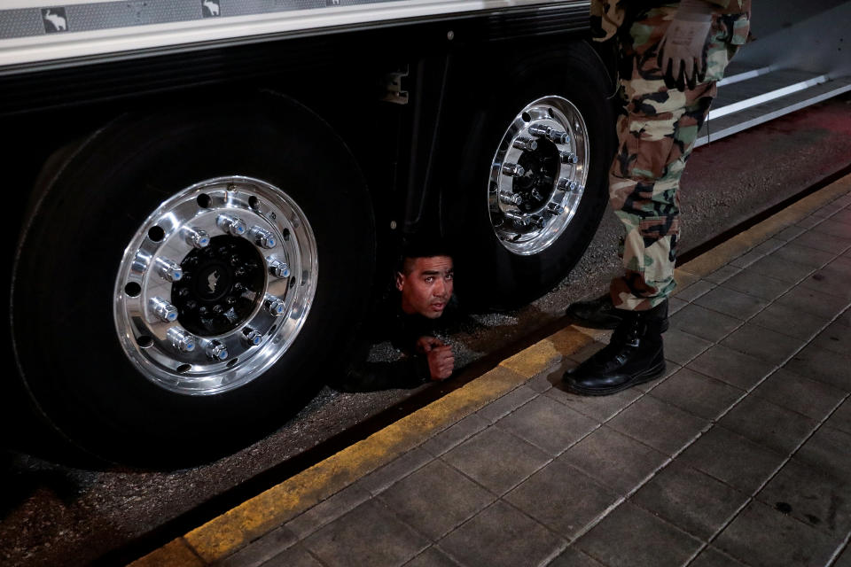 <p>Un inmigrante observa desde debajo de un camión mientras que un agente espera para deternele en Patras (Grecia). El fotógrafo recuerda que durante un control los policías estaban revisando un camión cuando de repente vieron a un inmigrante escondido en la parte inferior. Salió lentamente y fue detenido.<br>Foto: REUTERS/Alkis Konstantinidis </p>