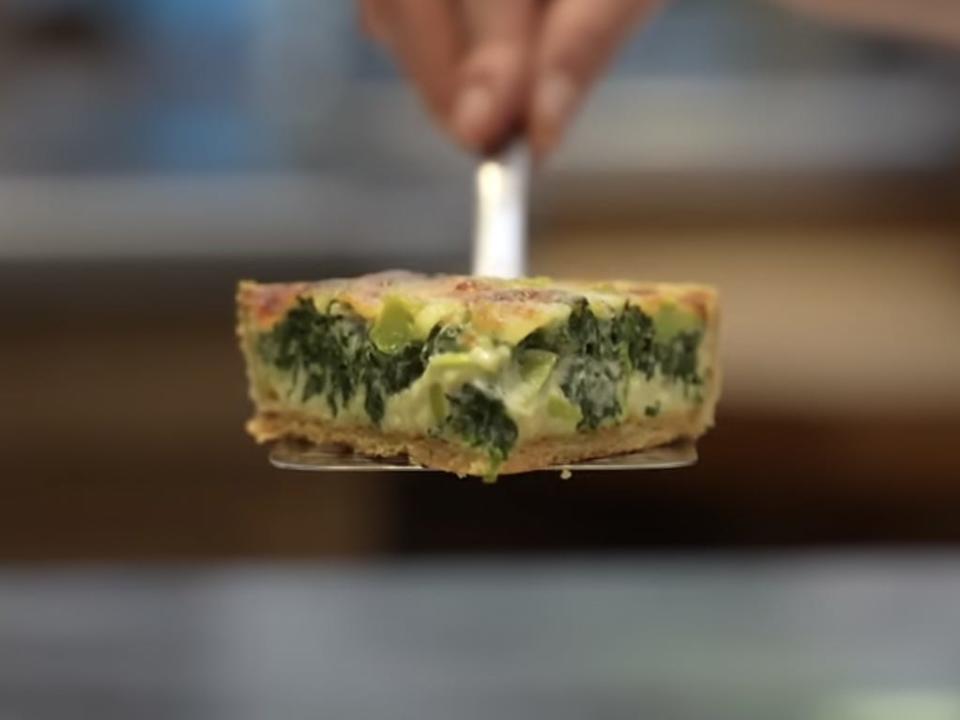 A screenshot from The Royal Family's video demonstration of Coronation Quiche, showing a slice lifted out of the dish.