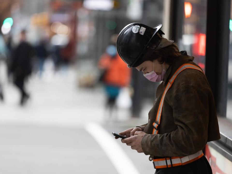 A masked construction worker uses his phone on Robson Street in Downtown Vancouver in January 2022.  (Andrew Lee/CBC - image credit)