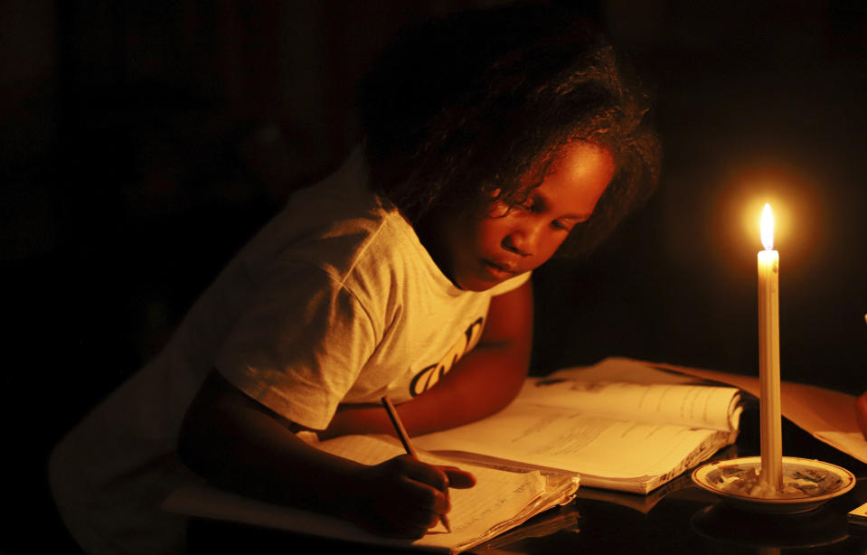 A child studies at home by candle light in Harare, Zimbabwe, Tuesday, Dec. 20, 2022. A buoyant holiday mood is not lifting the country which is coping with widespread power outages and the world's highest food inflation. (AP Photo)