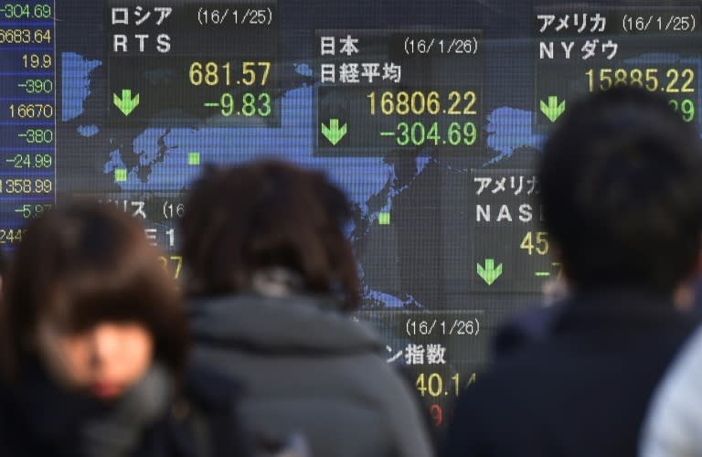 Pedestrians walk past a share prices board displaying movements on the Tokyo Stock Exchange