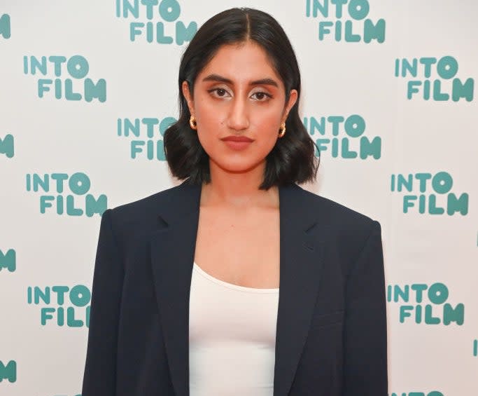 Person posing on the red carpet at an Into Film event, wearing a black blazer, white top, and blue jeans