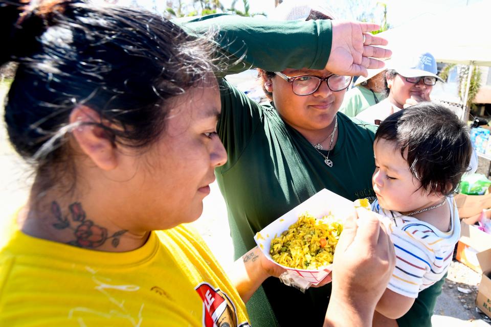 Amelia Cite, left, feeds her son Kevin Cite as Lonelli Francisco holds him as they pick up food, water and diapers dropped off by R2C2 volunteers at The Palms on Pine Island near Fort Myers, Fla., on Wednesday, Oct. 5, 2022.