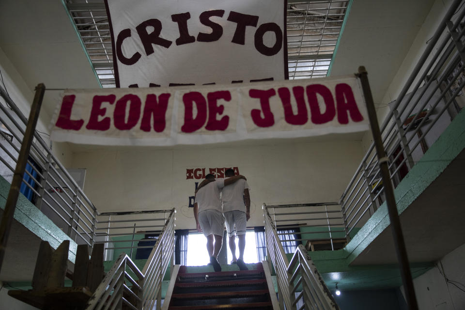 Inmates Ruben Luna, right, who is serving a 14-year sentence for murder, embraces Sebastian Monje, who has been in prison for eight months for attempted murder and robbery, before being baptized inside an evangelical cellblock at the penitentiary in Pinero, Argentina, Saturday, Dec. 11, 2021. The signs read in Spanish "Christ lives. Lion of Judah." (AP Photo/Rodrigo Abd)
