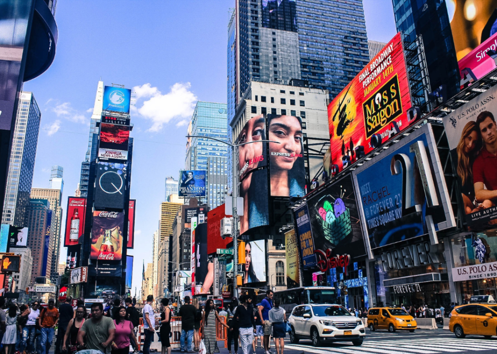 Tall skyscrapers with colorful ads, traffic and crowds of people. 