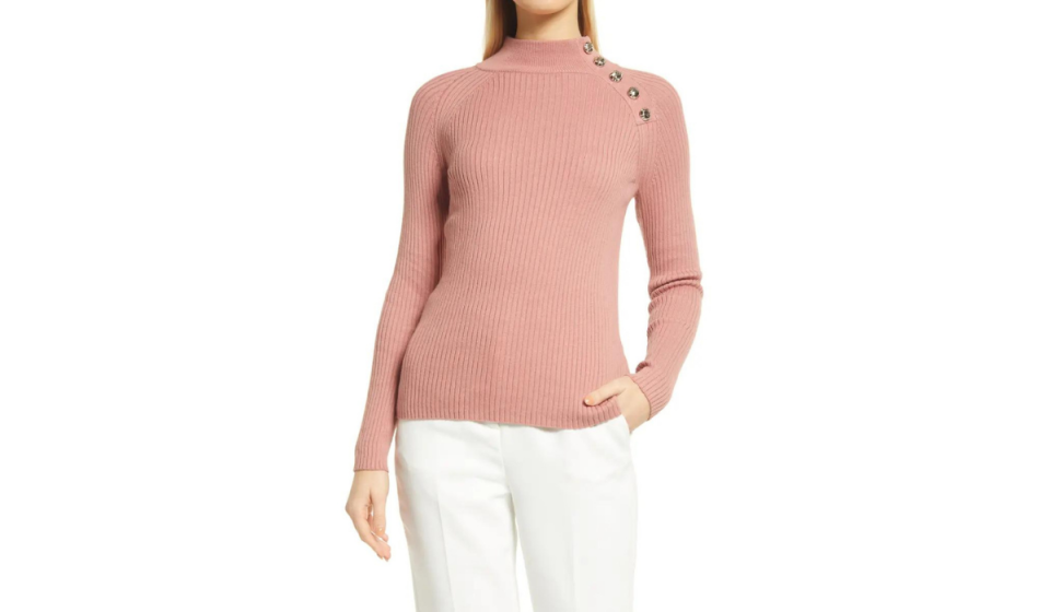 Blond woman wearing dusty rose colored sweater with white slacks. 