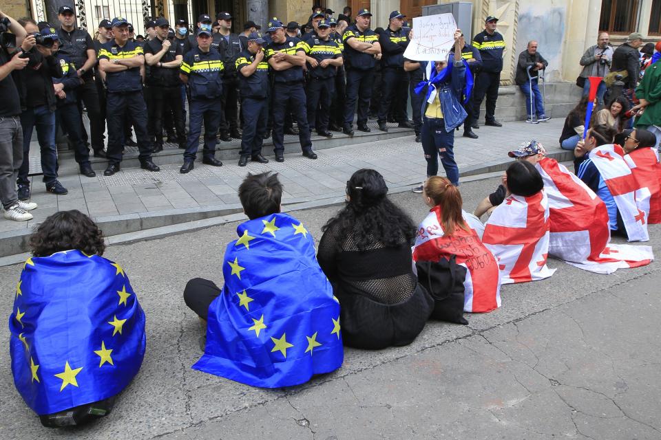 Demonstrators with Georgian national and EU flags sit in front of police during an opposition protest against the foreign influence bill at the Parliamentary building in Tbilisi, Georgia, Tuesday, May 28, 2024. (AP Photo/Shakh Aivazov)