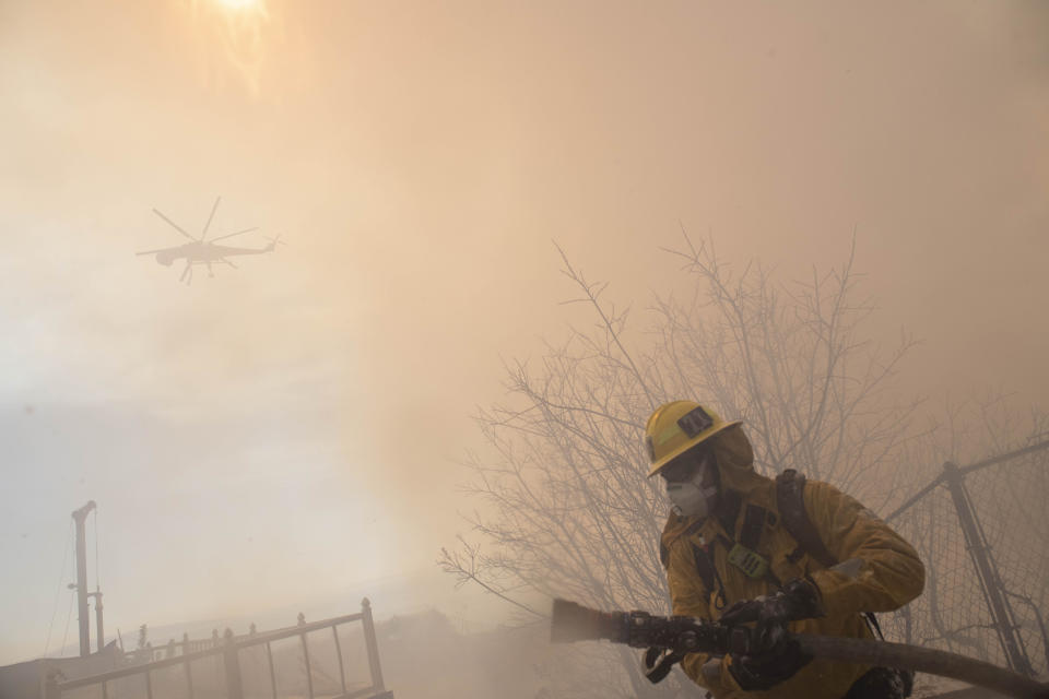 A firefighter carries a hose during work to protect homes from the flames of a wildfire in the Pacific Palisades area of Los Angeles, Monday, Oct. 21, 2019. (AP Photo/Christian Monterrosa)