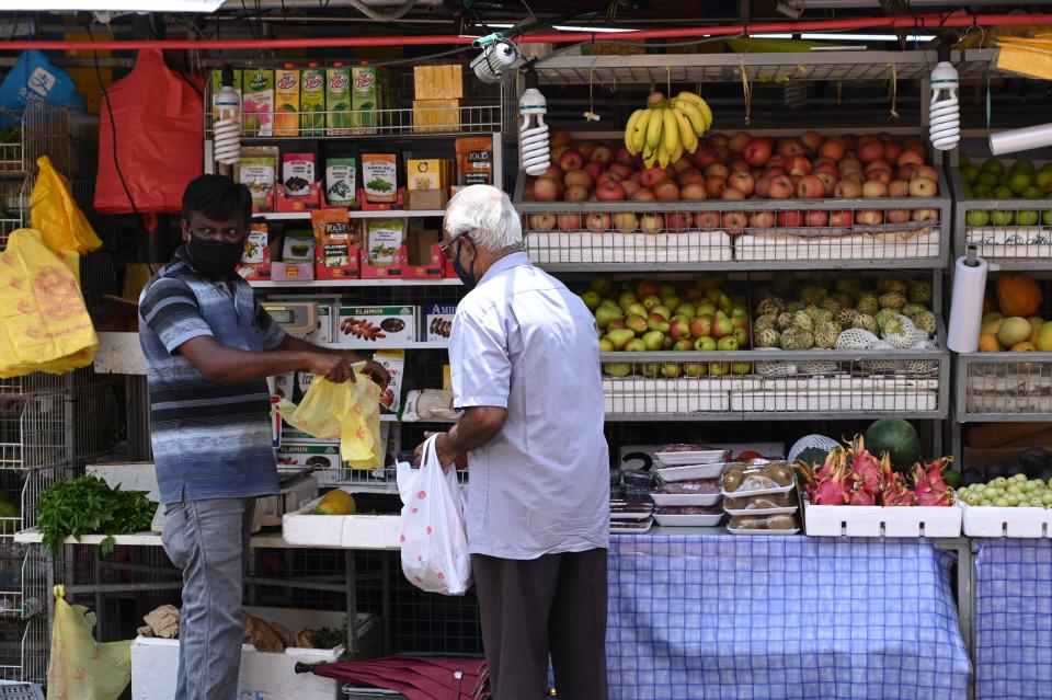 A vendor wearing a protective facemask amid fears about the spread of the COVID-19 coronavirus serves a customer at a fruit stall in Singapore on May 8, 2020. (Photo by ROSLAN RAHMAN / AFP) (Photo by ROSLAN RAHMAN/AFP via Getty Images)