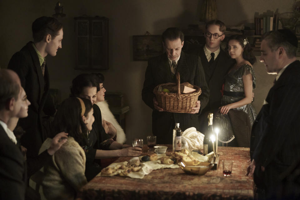 The Frank, van Pels, and Gies families celebrate Hanukkah in the upcoming limited series A Small Light. From left: Liev Schreiber as Otto Frank, Ashley Brooke as Margot Frank, Rudi Goodman as Peter van Pels, Billie Boullet as Anne Frank, Amira Casar as Edith Frank, Caroline Catz as Mrs. van Pels, Noah Taylor as Dr. Pfeffer, Joe Cole as Jan Gies, Bel Powley as Miep Gies, and Andy Nyman as Mr. van Pels. (Photo credit: National Geographic for Disney/Dusan Martincek)