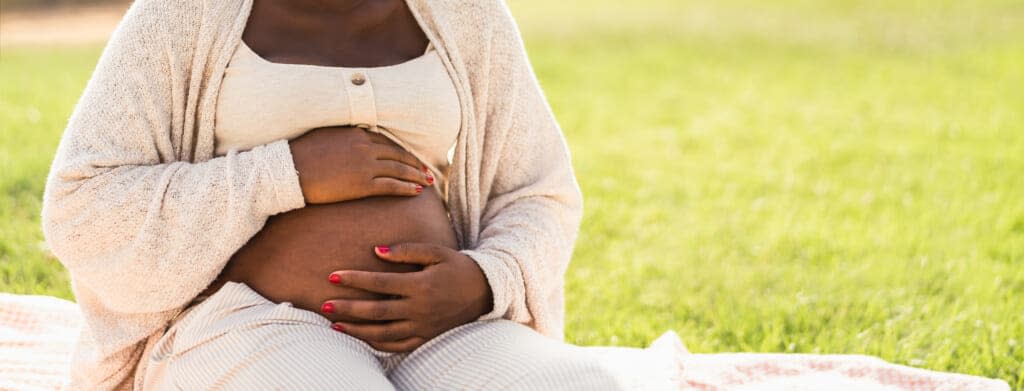 Close up pregnant belly of young African woman sitting in park – Maternity lifestyle concept