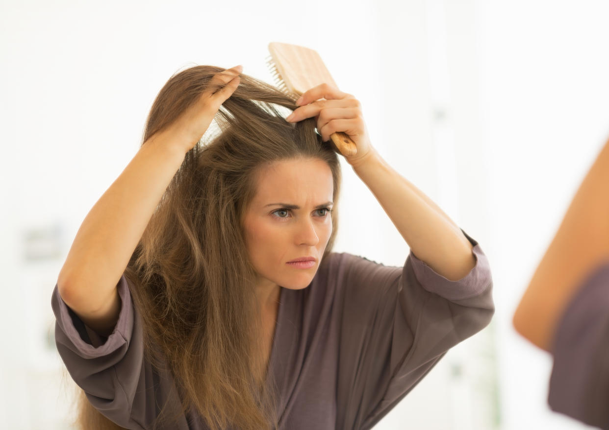 Concerned young woman combing hair in bathroom