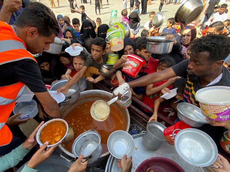 Palestinos, que huyeron de sus casas debido a los ataques israelíes, se reúnen para recibir su parte de alimentos de caridad, en Rafah