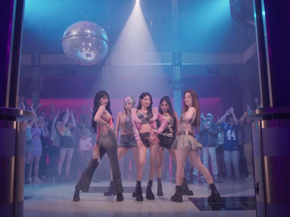 minni, yuqi, miyeon, soyeon, and shuhua in the performance music video for queencard, posing in the center of a dance floor as people clap and cheer around them