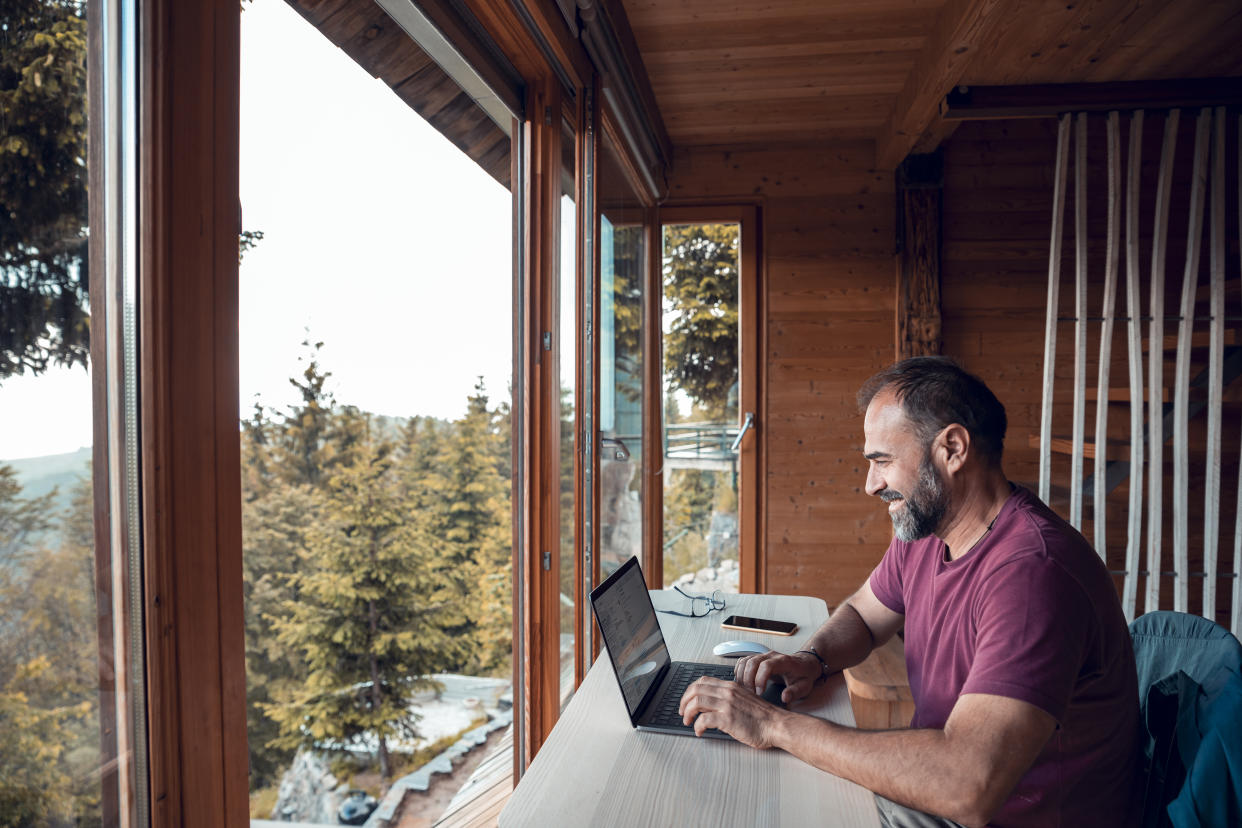 Close up of a mid adult man working on a laptop from his cabin in the woods