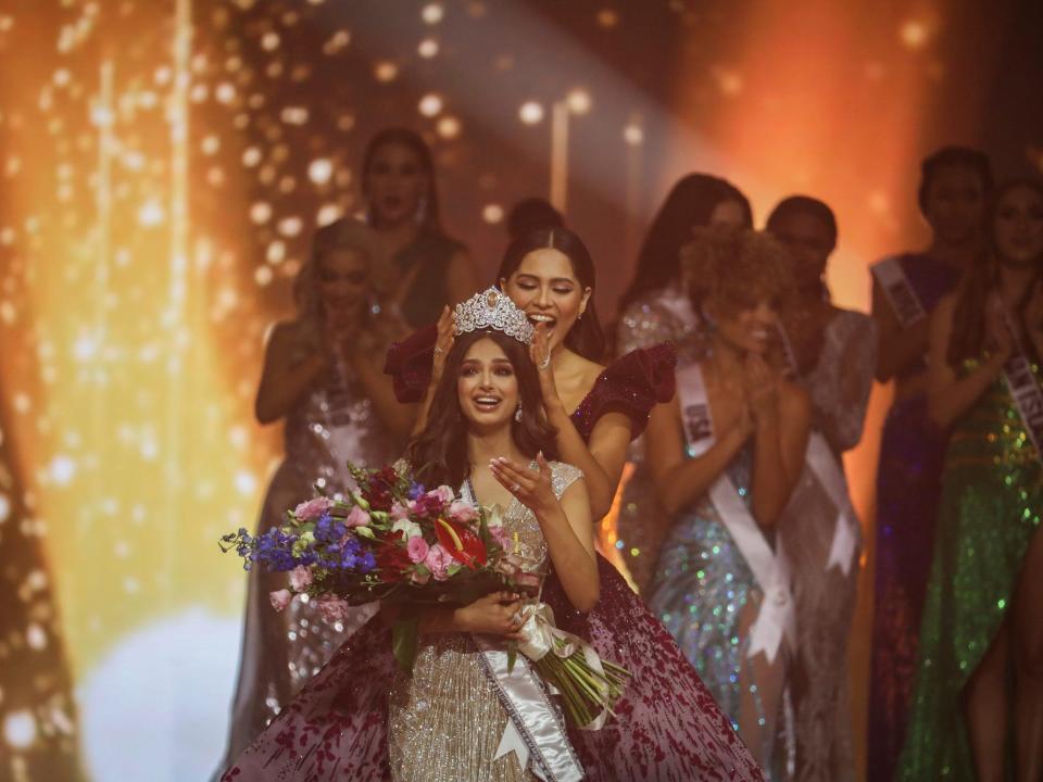 Miss Universe 2021 is crowned as she holds a bouquet of flowers and sparklers erupt.