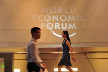 People walk past a logo at the World Economic Forum in Dalian, Liaoning province, China, June 27, 2017. Picture taken June 27, 2017. CNS/Yu Haiyang via REUTERS