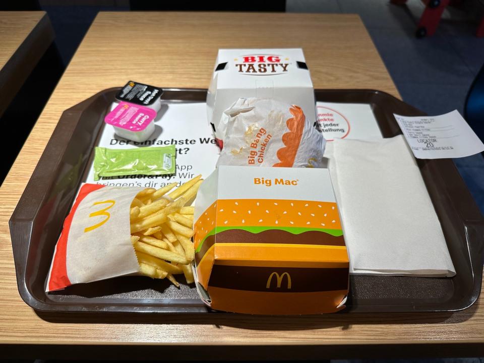 mcdonalds order three packaged sandwiches, french fries in a paper bag, three sauce packets and napkins on a brown tray on a wood table