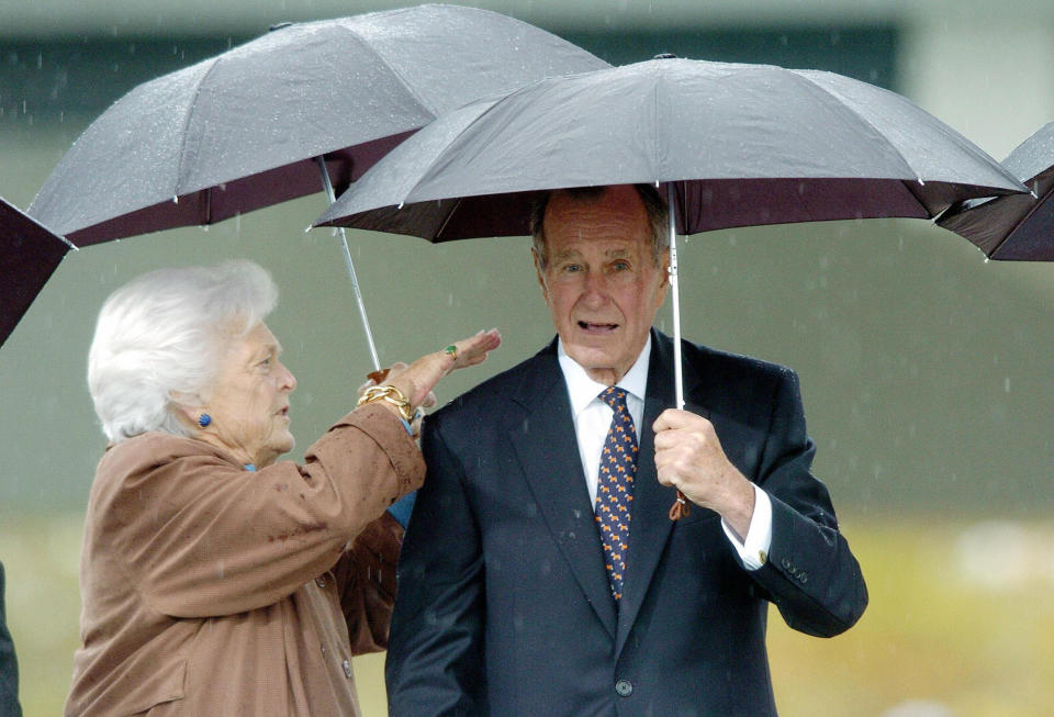 Barbara Bush wipes water off the shoulder of her husband former President George H.W. Bush during the inauguration of the William J. Clinton Presidential Center in Little Rock, Arkansas, on Nov. 18, 2004.