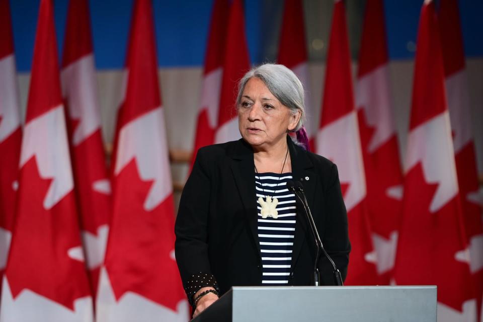 Simon stands behind a podium in front of Canada Flags