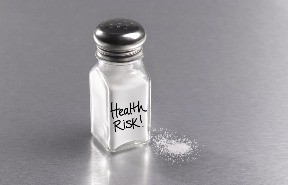 Salt shaker on a table with "Health Risk!" written on it, some salt spilled beside it
