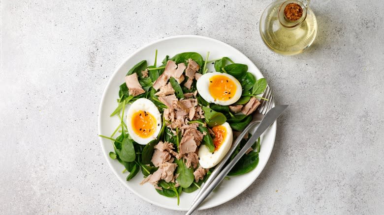 Canned tuna on spinach with eggs on a plate with a knife and fork