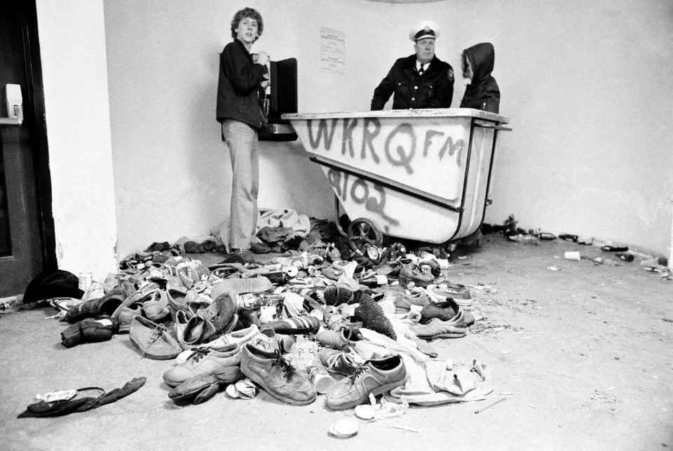 FILE - In this Dec. 3, 1979 file photo, concert-goers and a policeman stand with a pile of shoes and clothing which were left after a crowd surged toward doors to Cincinnati's riverfront coliseum to get into a rock concert by British rock band The Who, in Cincinnati, Ohio. Eleven fans where killed in the tragedy. (AP Photo/Brian Horton, File)