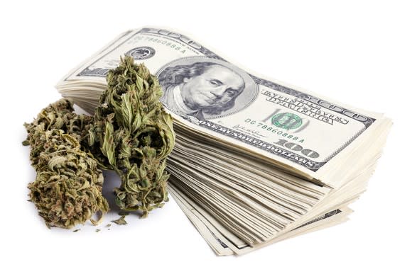 Marijuana buds next to a stack of $100 bills.