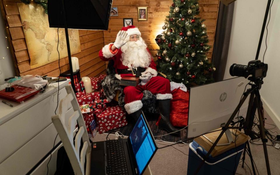 Aaron Spenedelow dressed as Santa Claus waves to the camera during a Zoom call with a family, as Santa's Grotto Live gets underway in Wembley, north London - NIKLAS HALLE'N/AFP