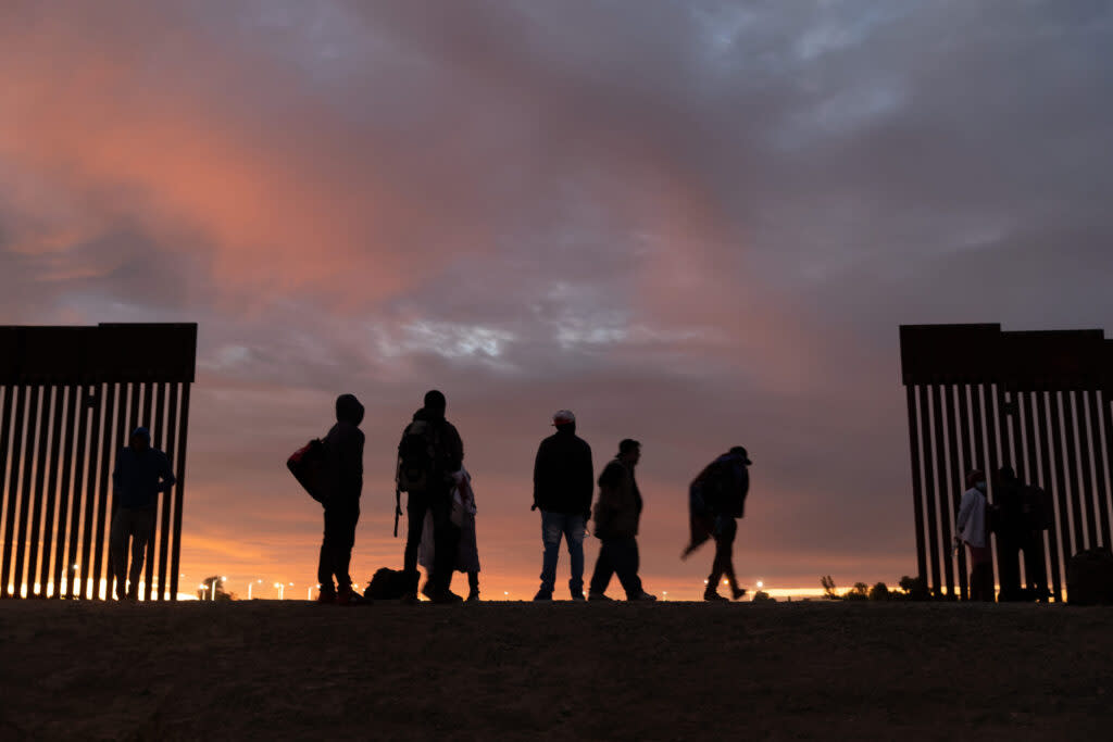 immigrants stand at a gap in the border wall in Yuma, Arizona